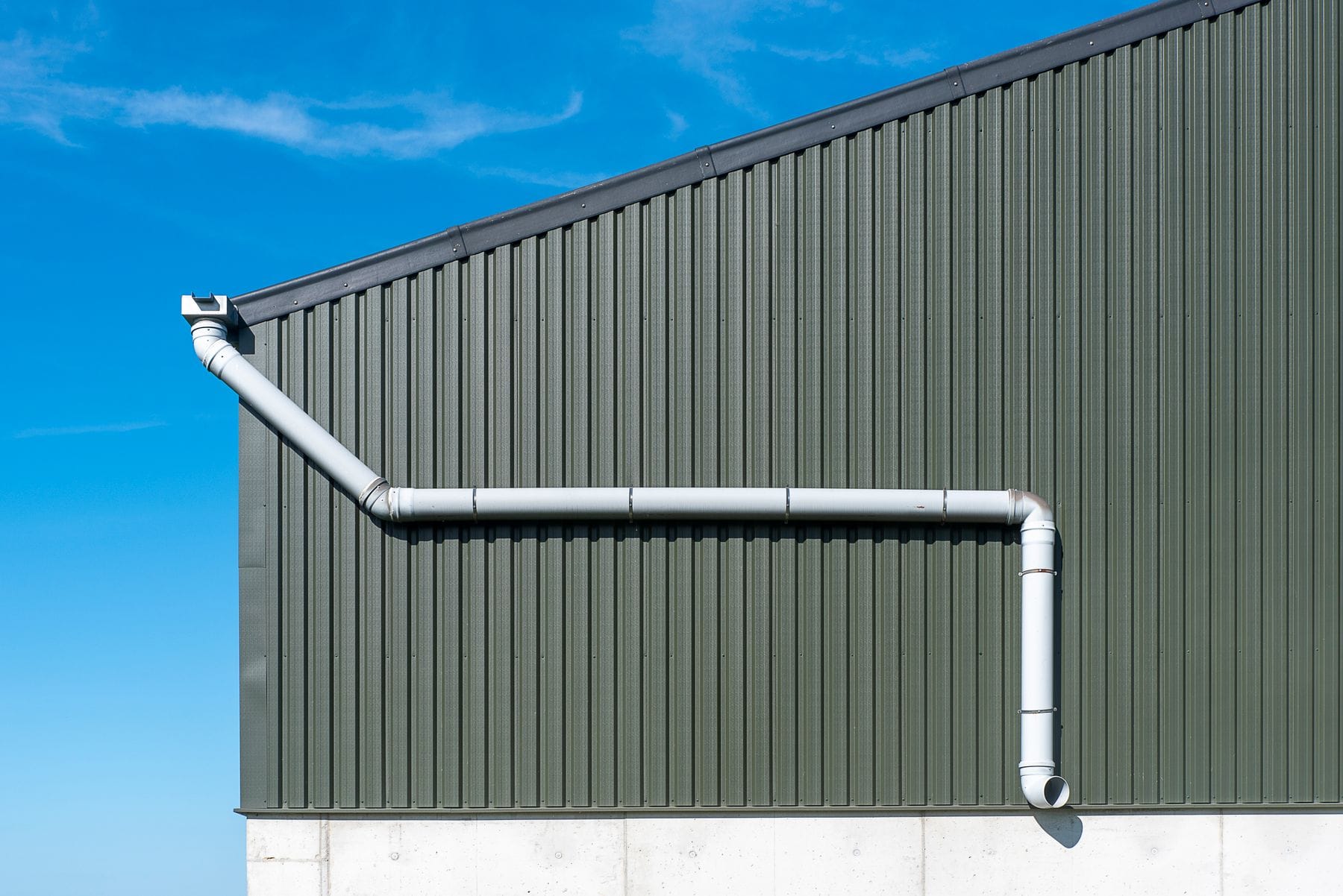 Steel-clad building wall with a downspout for roof drainage