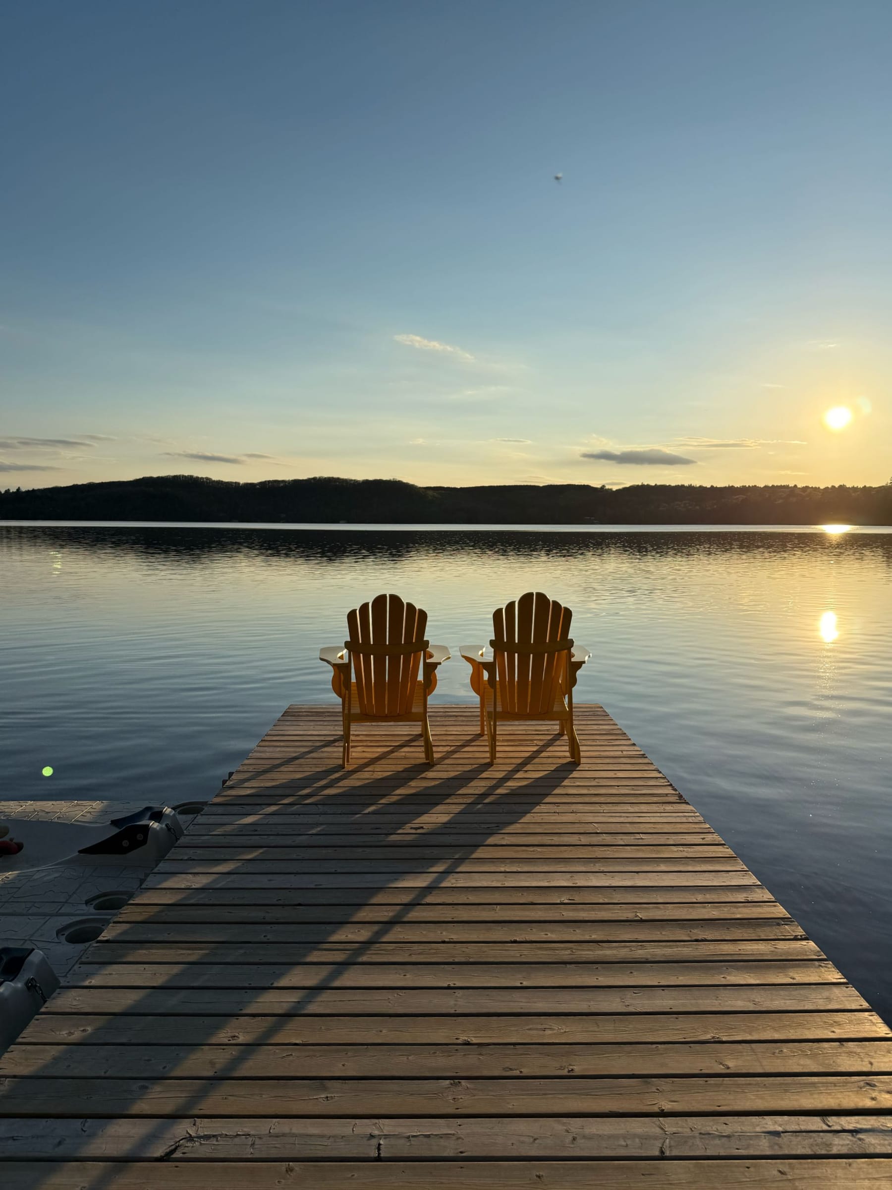 Two Adirondack chairs on a wooden dock at sunset over a calm lake